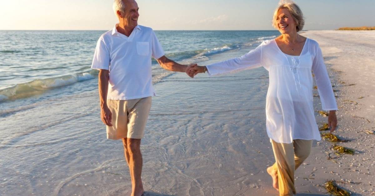 An older couple walks hand-in-hand on the beach.