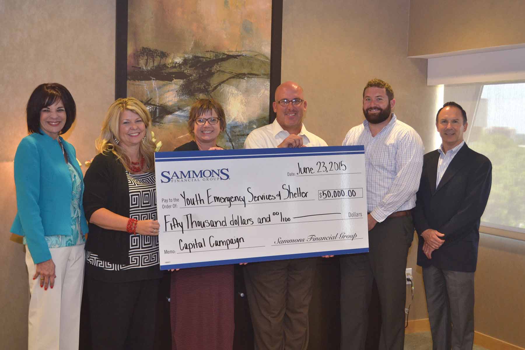 A group photo of Sammons Financial Group employees holding a $50,000 check donated to Youth Emergency Services and Shelter.