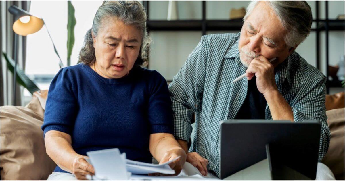 An older husband and wife look concerned while reviewing documents together.