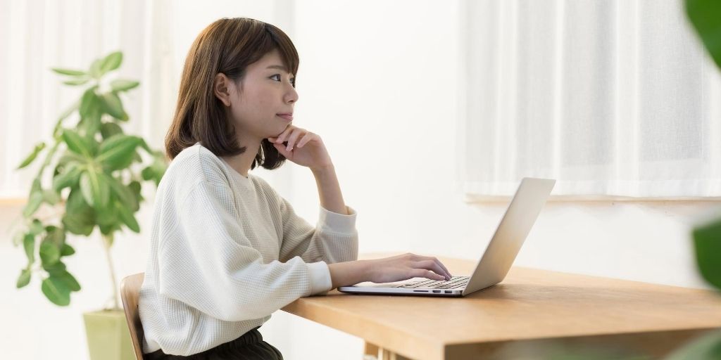 A young Asian woman looks worried while using a computer.