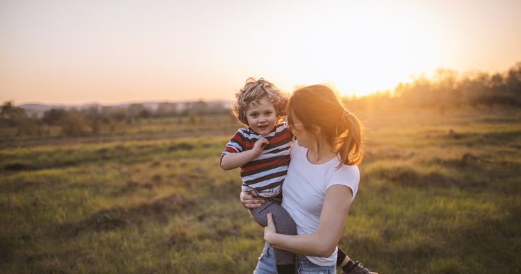 A mother holds son walking in an open field.