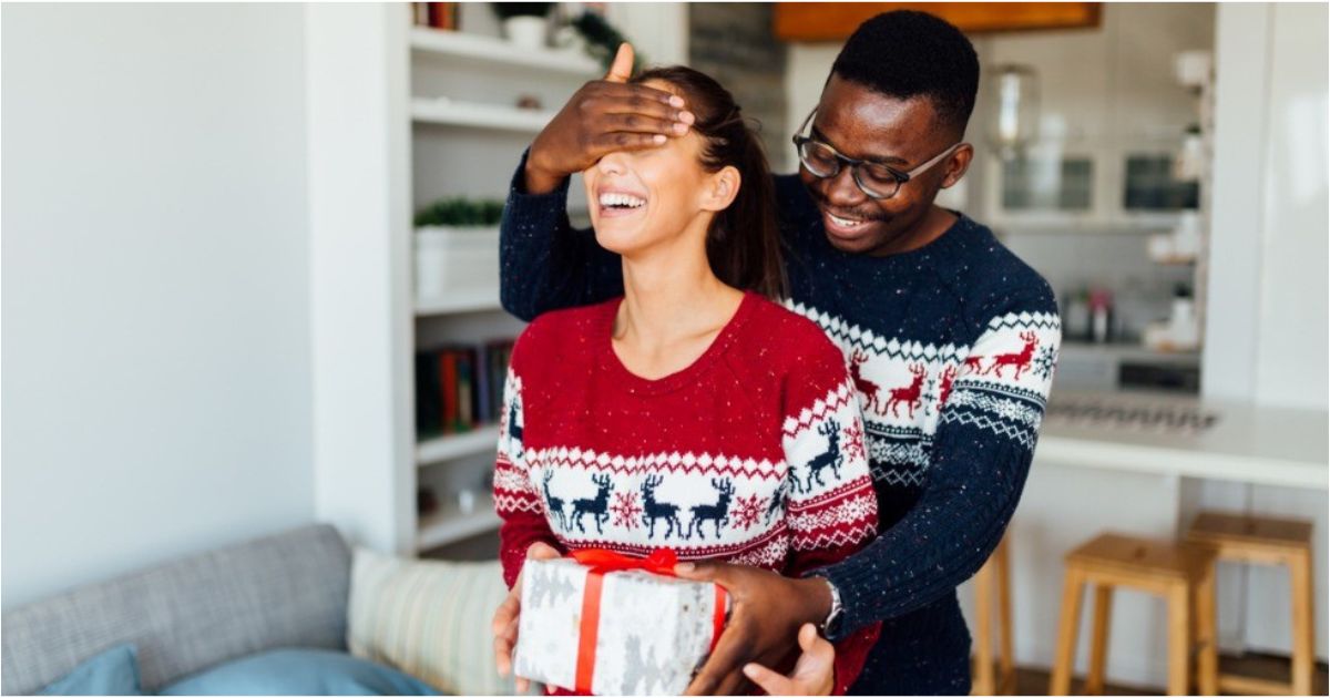 A man covers his girlfriends eyes before giving her a holiday gift.