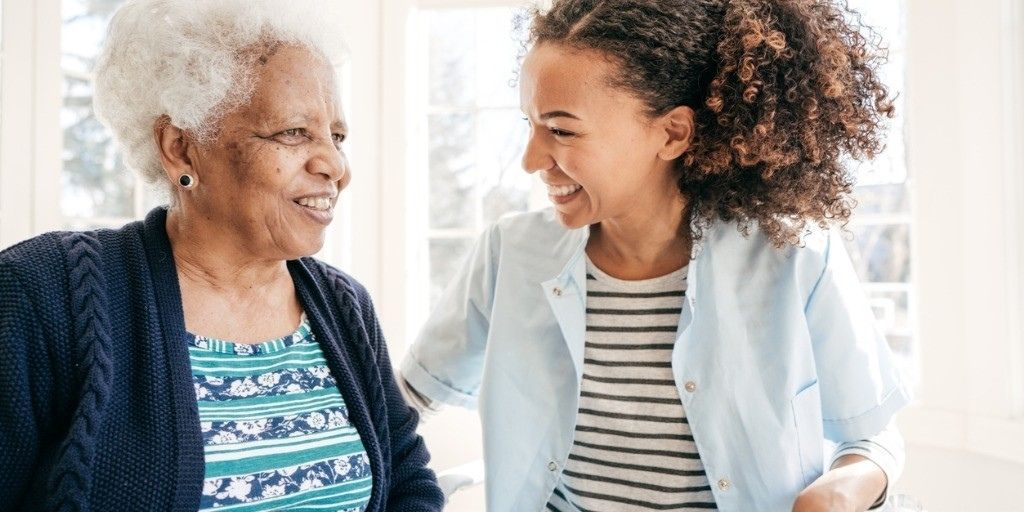 A young woman smiles and the elderly woman she cares for