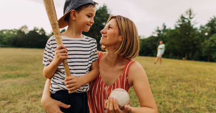 A woman holds a baseball while smiling at her shot holding a baseball bat.