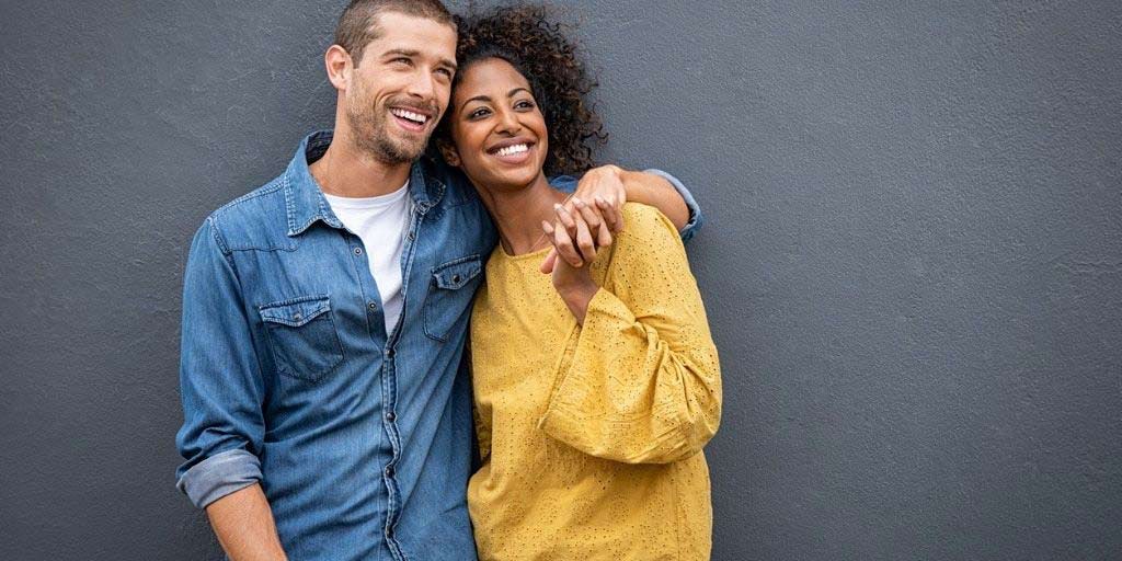 A young biracial couple embrace while flashing big smiles