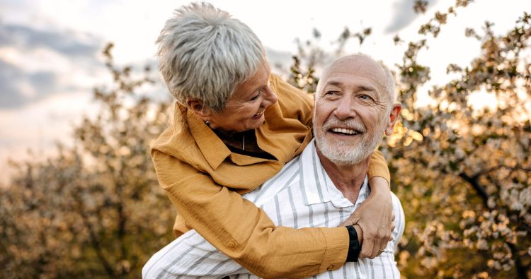 An older couple walk through an orchard together.