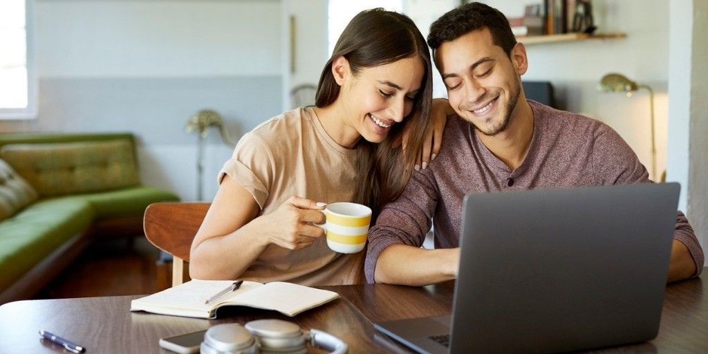 A young couple sip coffee while researching life insurance on their laptop
