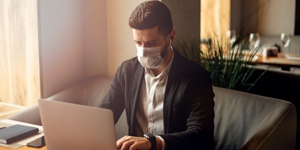 A young man wearing a medical mask works on his computer