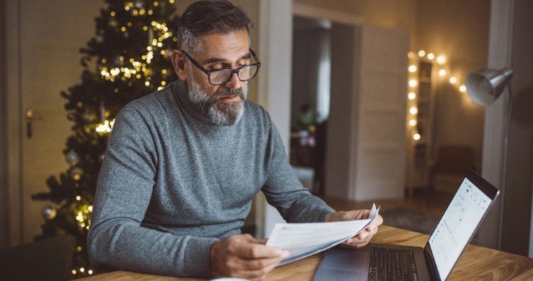 A man reviews financial documents and bills on his computer.