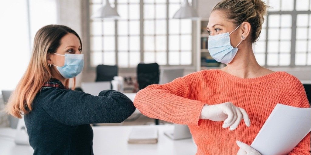 Two women wearing masks bump elbows