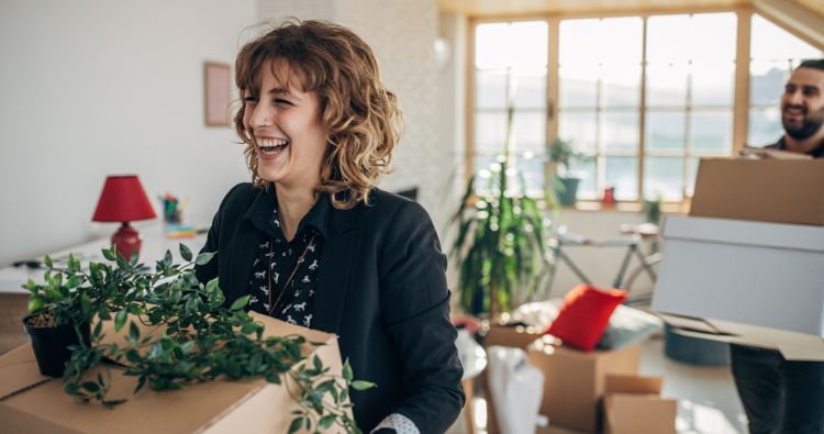 A woman walks through her new place holding a cardboard box.