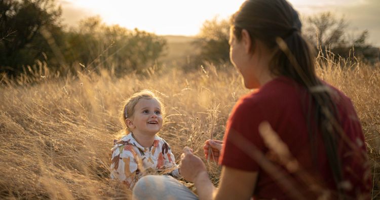A mother sits with her daughter in tall grass.