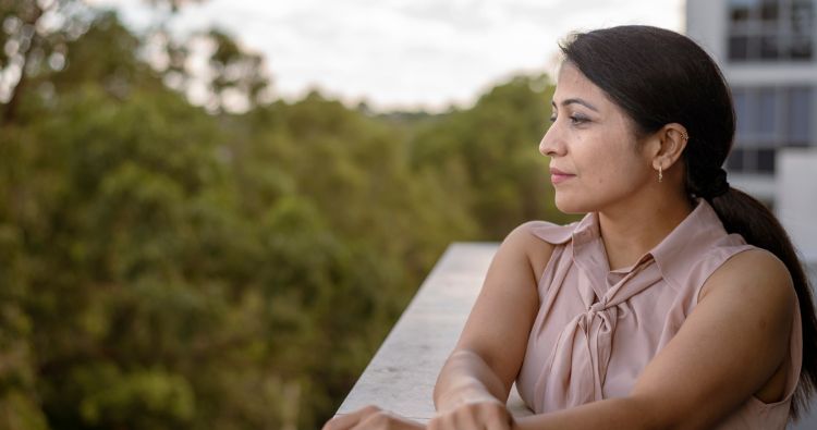 A woman on a balcony looks out at a forest.