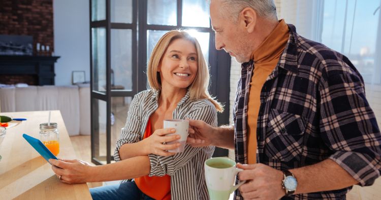 Smiling mature couple drinking coffee together in their kitchen while discussing financial plans