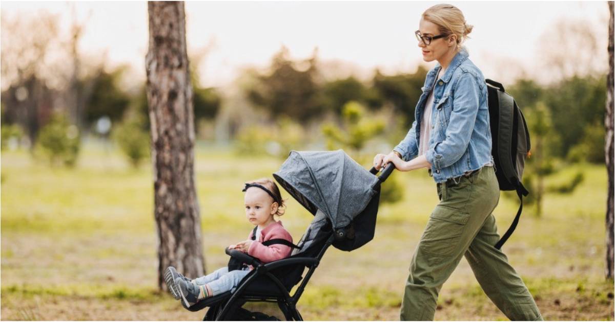 A young mother pushes her baby in a stroller while walking in the park.