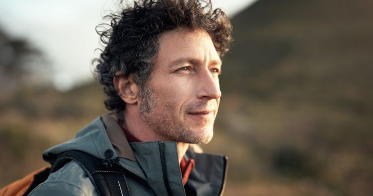 A man on a hike looks out at the landscape somberly.