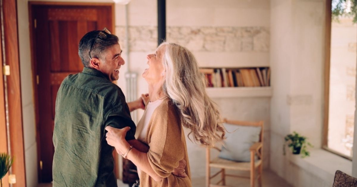 A retiree couple laugh together while dancing