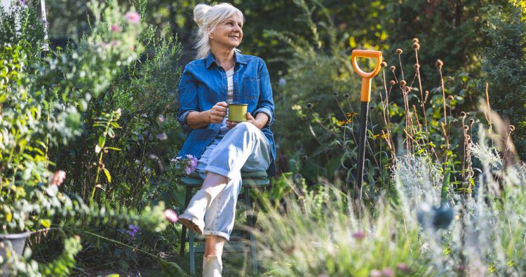 A retired women sits in her garden enjoying a cup of coffee.