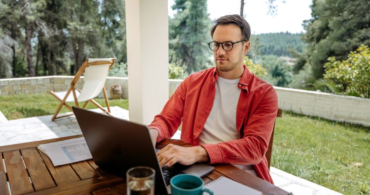 A man works on his computer outside on his porch.