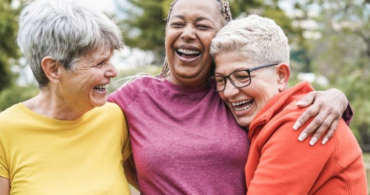 A group of retired women embrace while smiling.