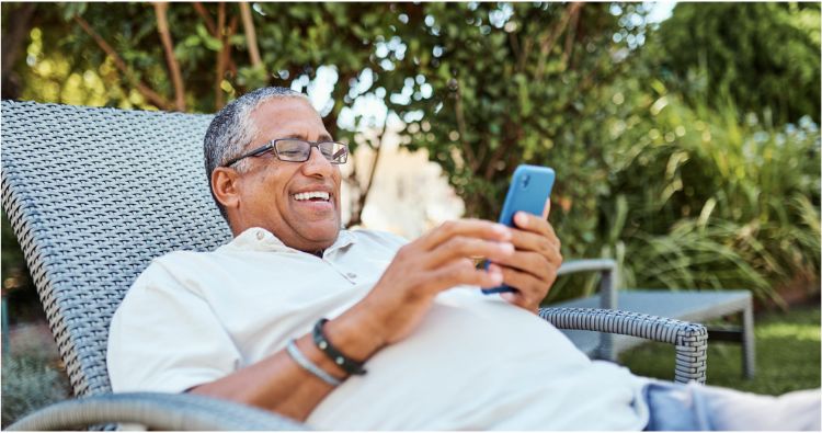 A man leans back in his chair smiling while looking at his phone