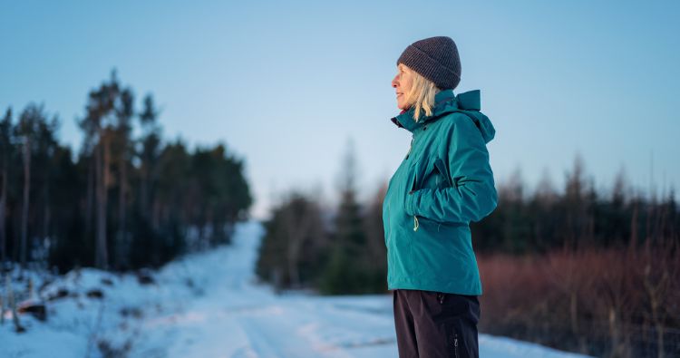 An older woman in winter gear pausing to look out over a snowy path