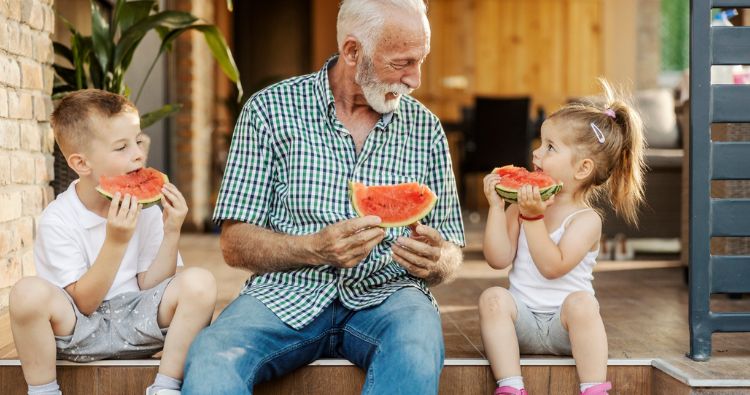 A grandpa enjoys slices of watermelon with his grandkids.