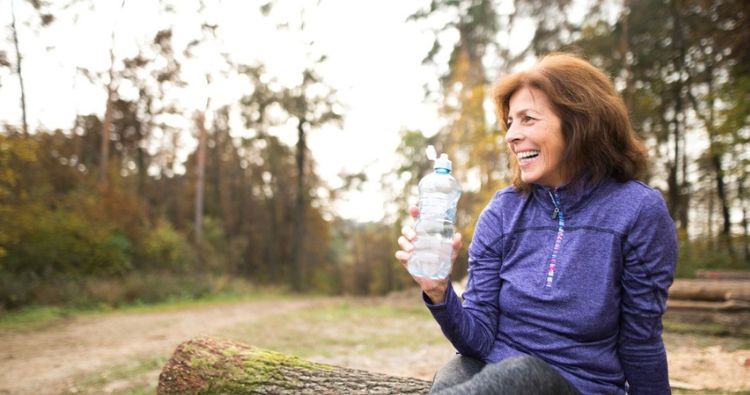 A retirement-aged woman drinks from a water bottle after a run.