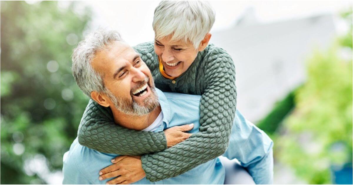 A retired woman smiles while her husband gives her a piggyback ride.