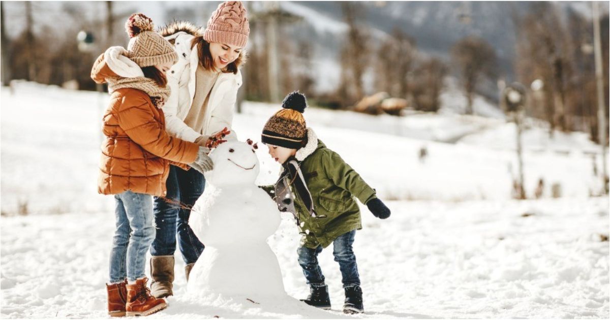A young family work together to build a snowman