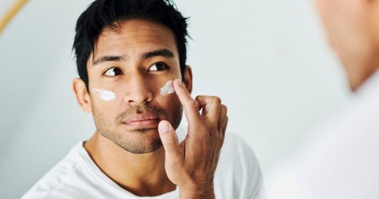 A man applies sunscreen to his face.