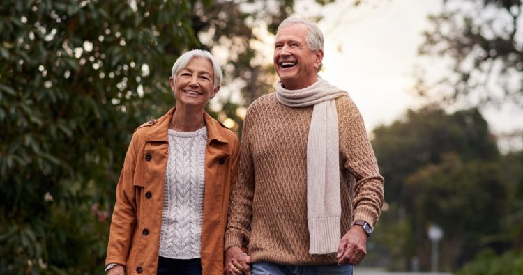 A ret0rement-aged couple walk hand-in-hand in the park.