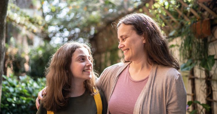 A mother walks with her teen daughter through a garden
