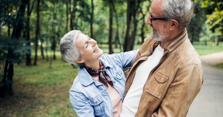 A retired couple embrace while they take a walk in the park