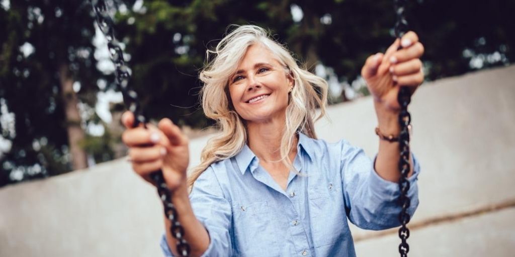 An older white retirement-aged women smiles while swinging.