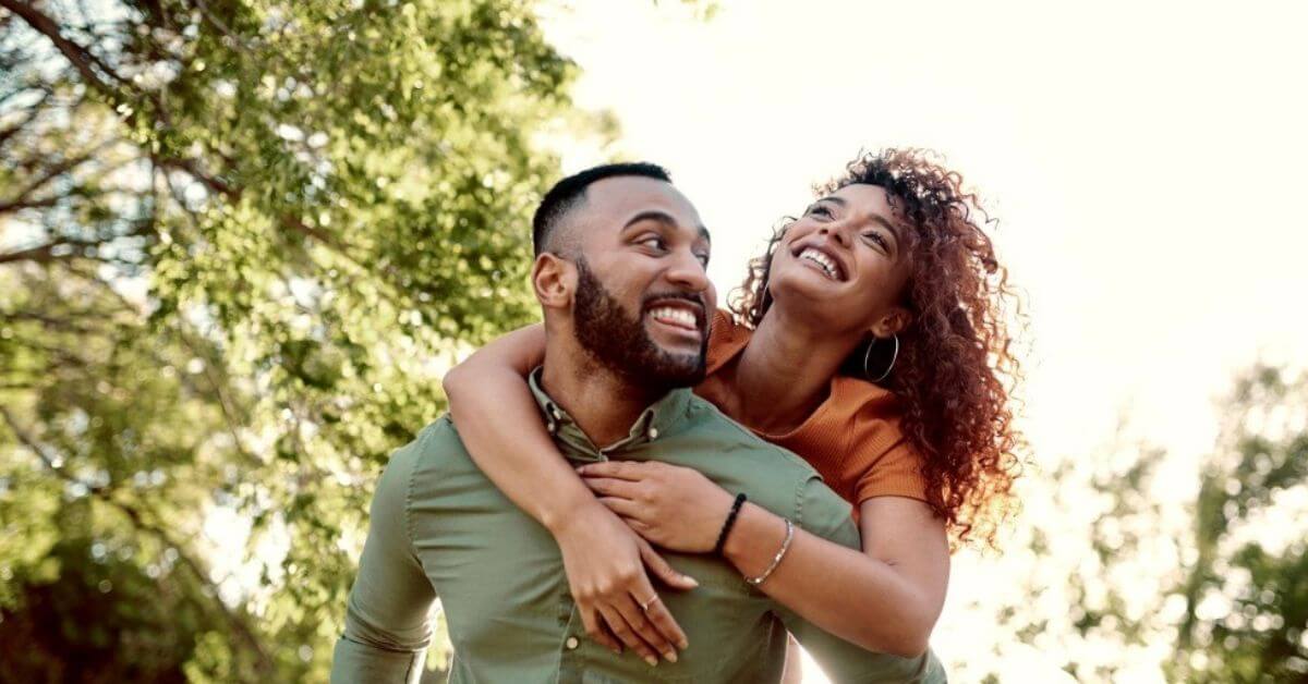 A young couple laugh while the man gives his partner a piggy-back ride.