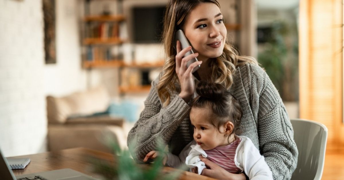 A young mother holds her daughter as she talks on the phone.