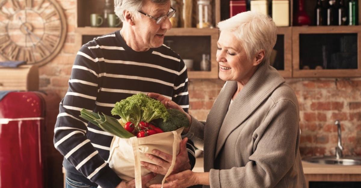 An older couple place groceries in a reusable bag to be sustainable.